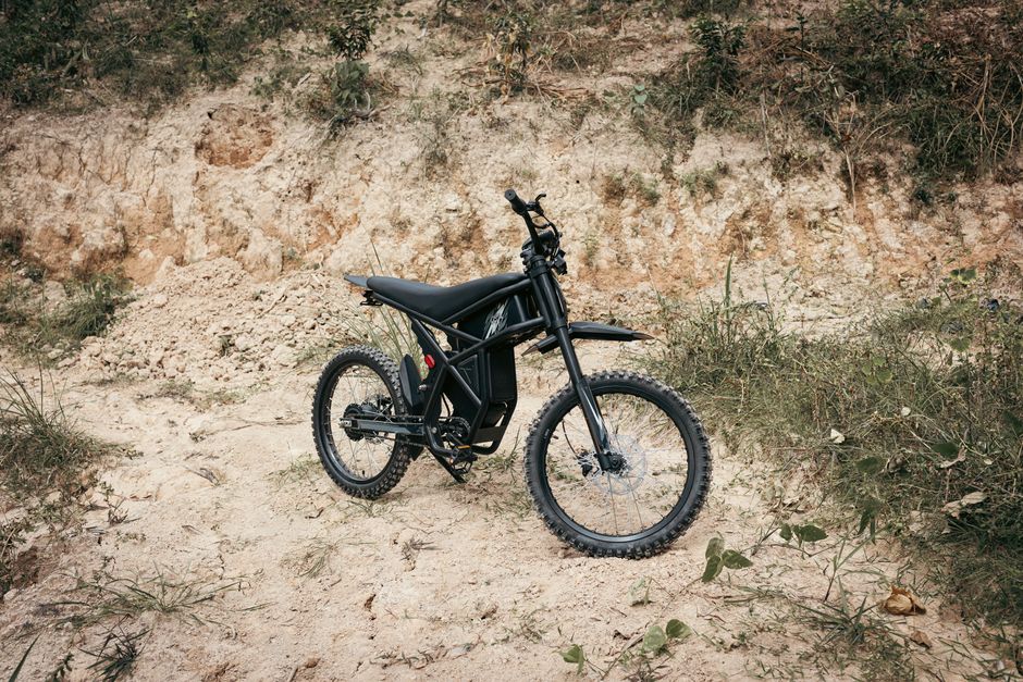 A black electric dirt bike parked on rocky outdoor terrain.