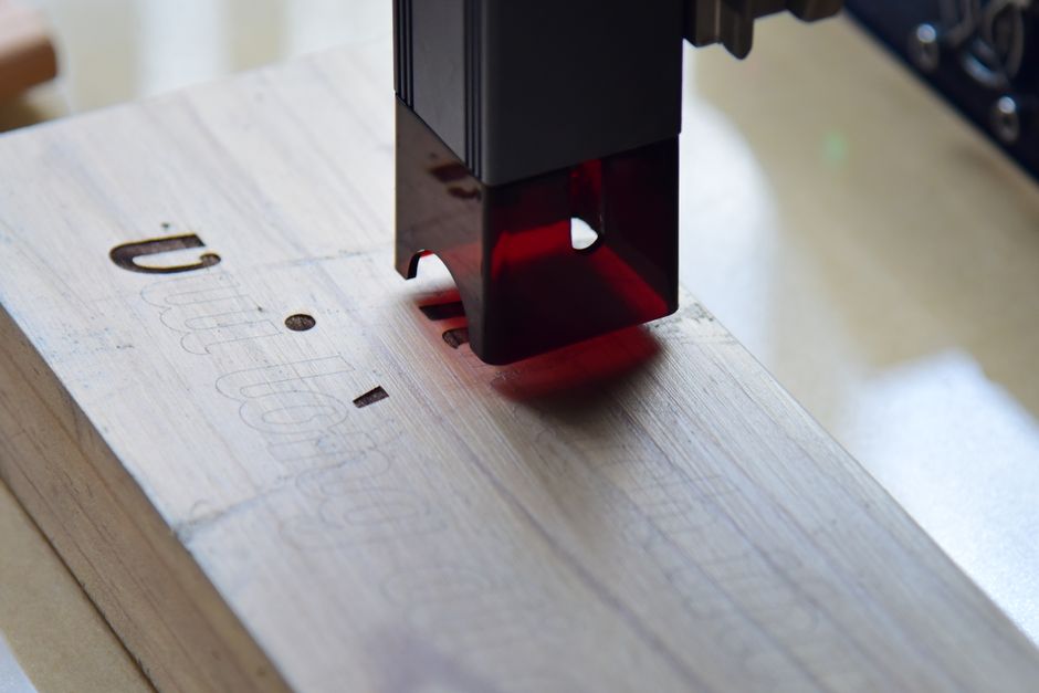 A laser module engraving lettering into a wooden board, with the beam visible at the head.